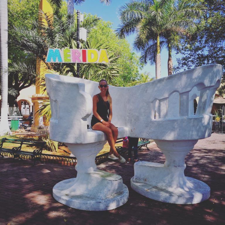 Sitting on a white confidante love seat by the Mérida sign